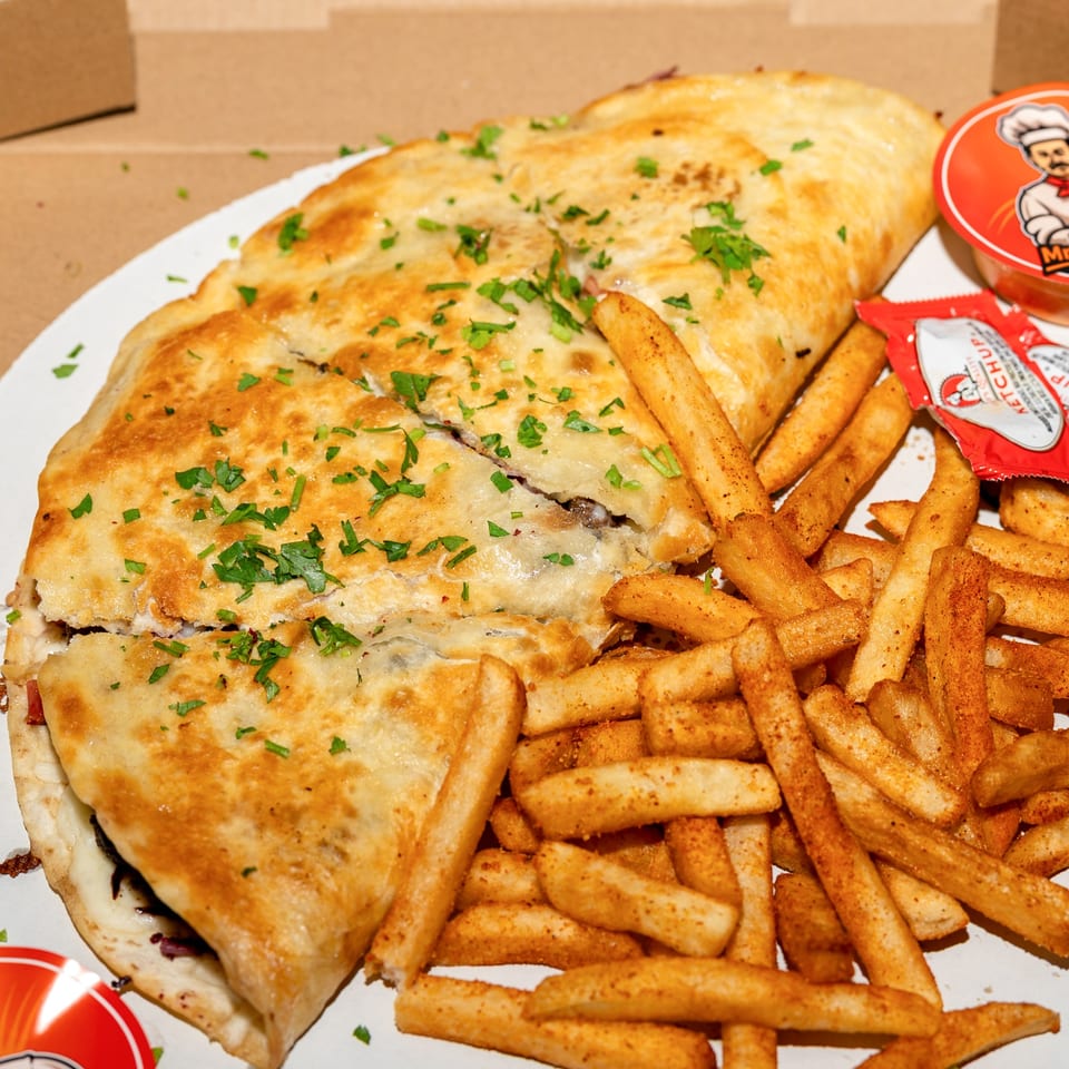 Golden-brown calzone topped with parsley, served with seasoned fries and ketchup packets.