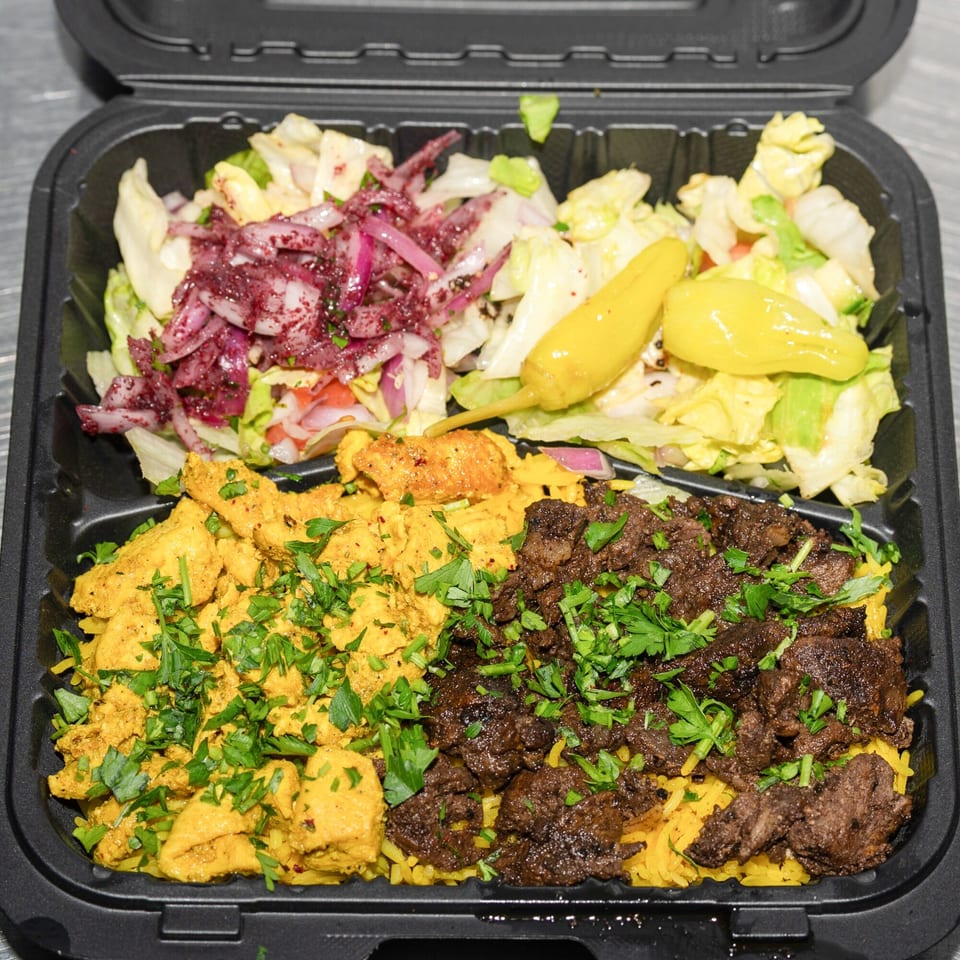 A black takeout container with chicken and beef over rice, and a side salad with pickled onions.
