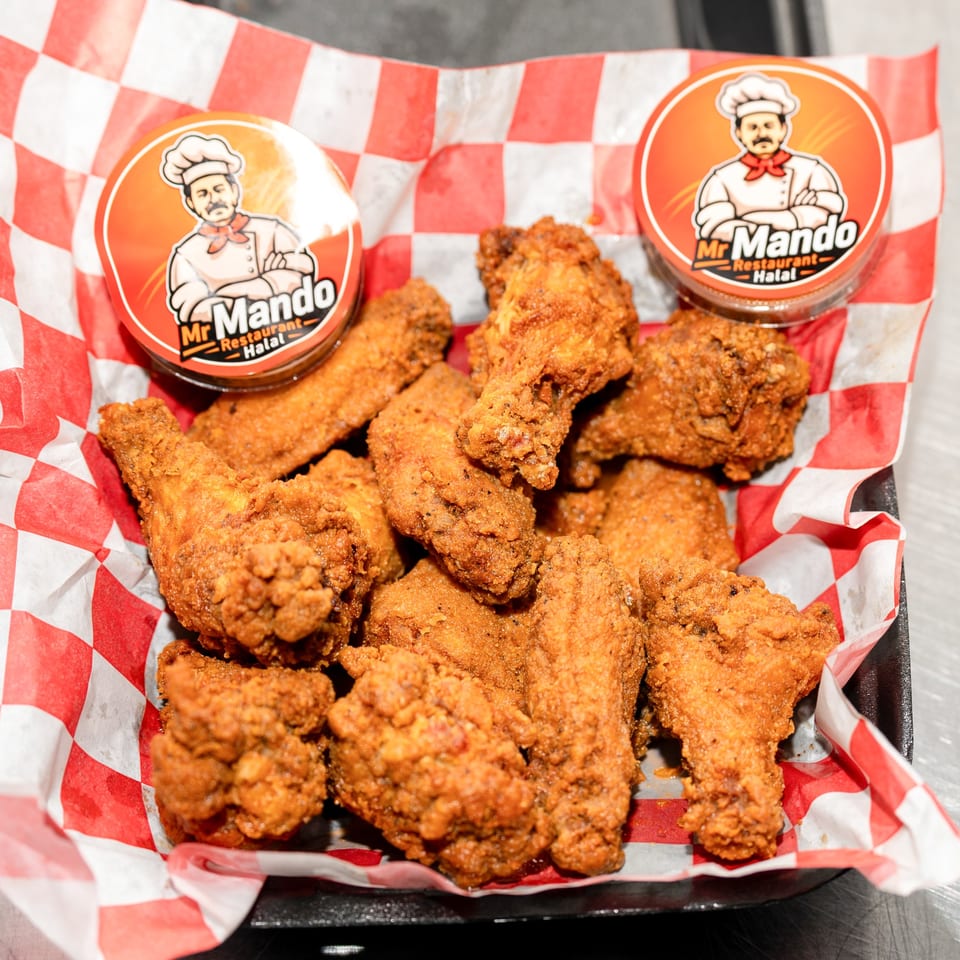 Crispy fried chicken wings in a red and white checkered paper-lined basket with two Mr. Mando sauce cups.