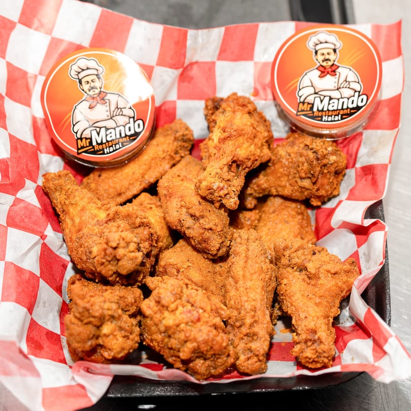 Crispy fried chicken wings in a red and white checkered paper-lined basket with two Mr. Mando sauce cups.