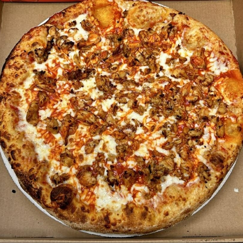 A whole buffalo chicken pizza with white cheese and orange sauce in a cardboard box.