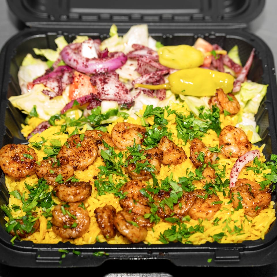 Shrimp and yellow rice with parsley, served in a black container with a side salad.