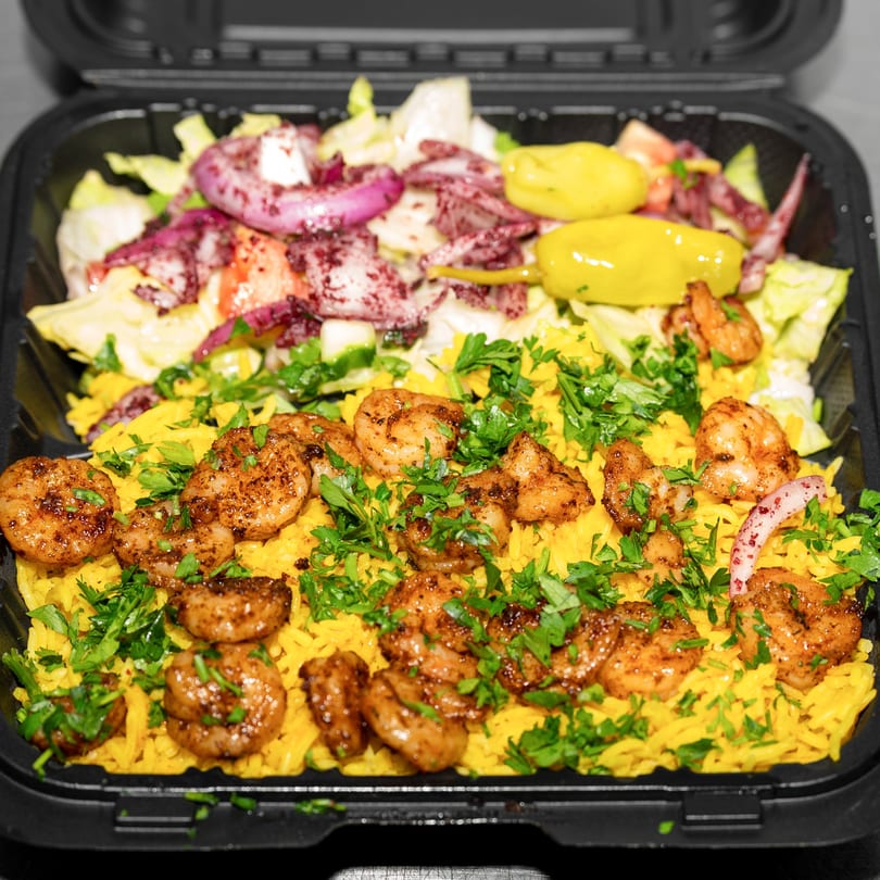 Shrimp and yellow rice with parsley, served in a black container with a side salad.