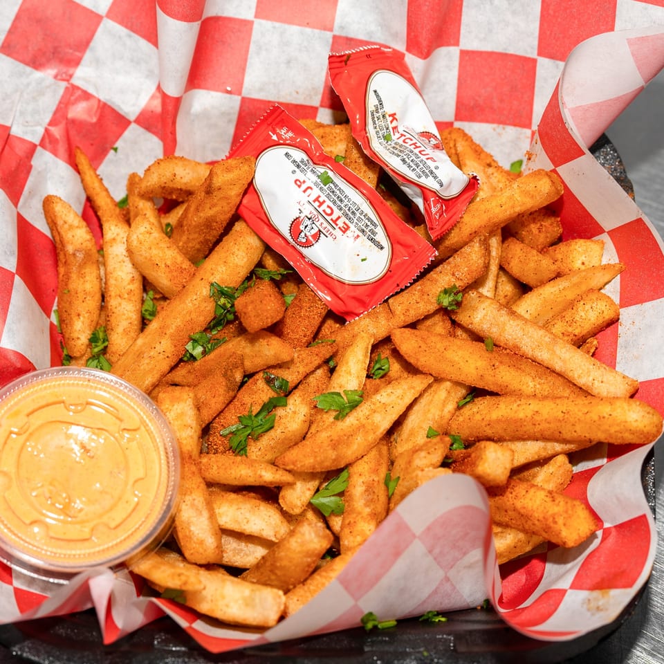 Seasoned french fries in a red and white checkered paper-lined basket with ketchup packets and dipping sauce.